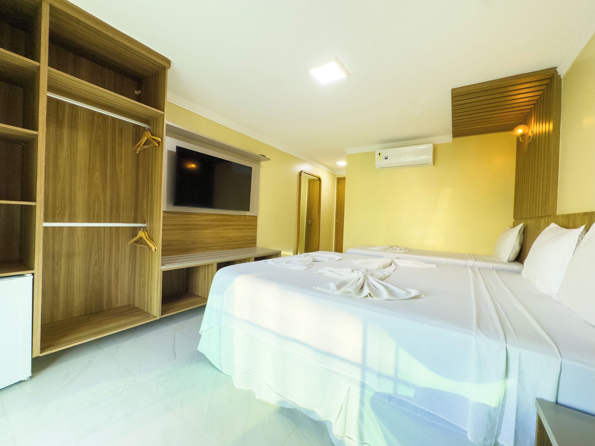 Habitación de hotel con una cama grande, televisor montado en la pared y un armario de madera.