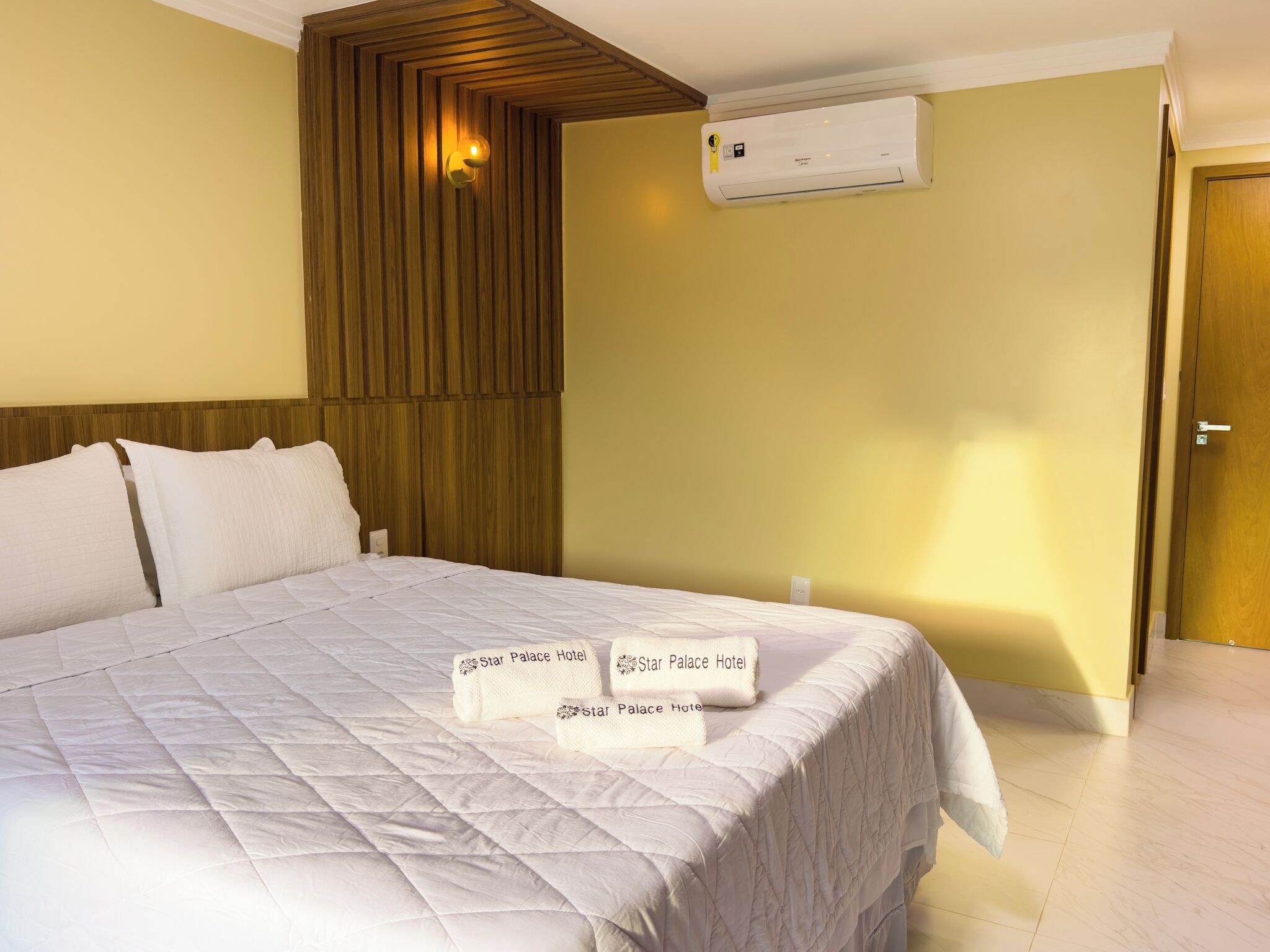 A hotel room with a large bed, a wall-mounted air conditioner, and a wooden headboard.