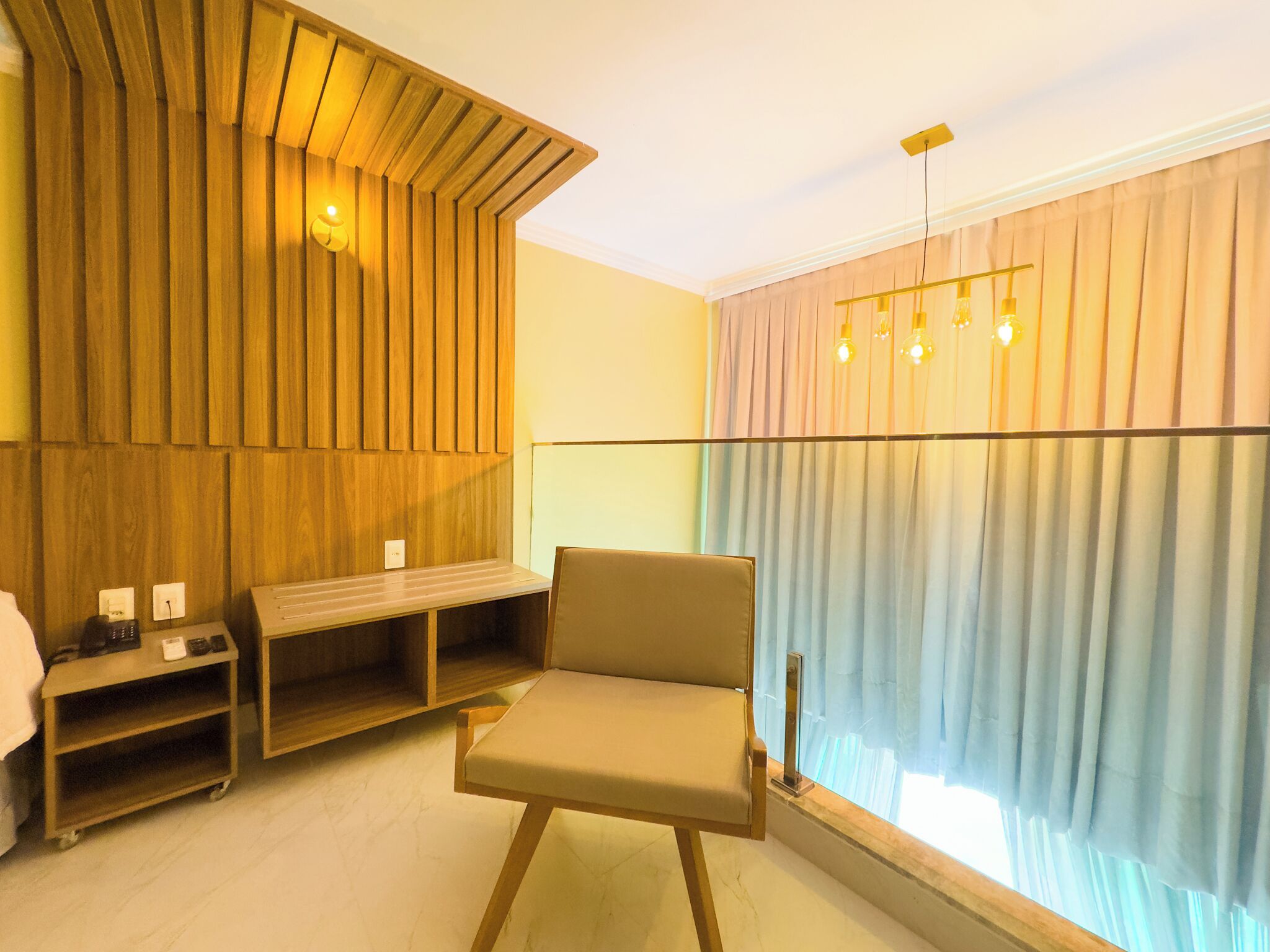 Ein modernes Zimmer mit einer Wand in Holzoptik, einem gepolsterten Sessel, einer Bank und einem Fenster mit Vorhängen.