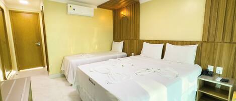 A hotel room with two beds, a wooden headboard, a small bedside table with a phone, and an air conditioning unit on the wall.