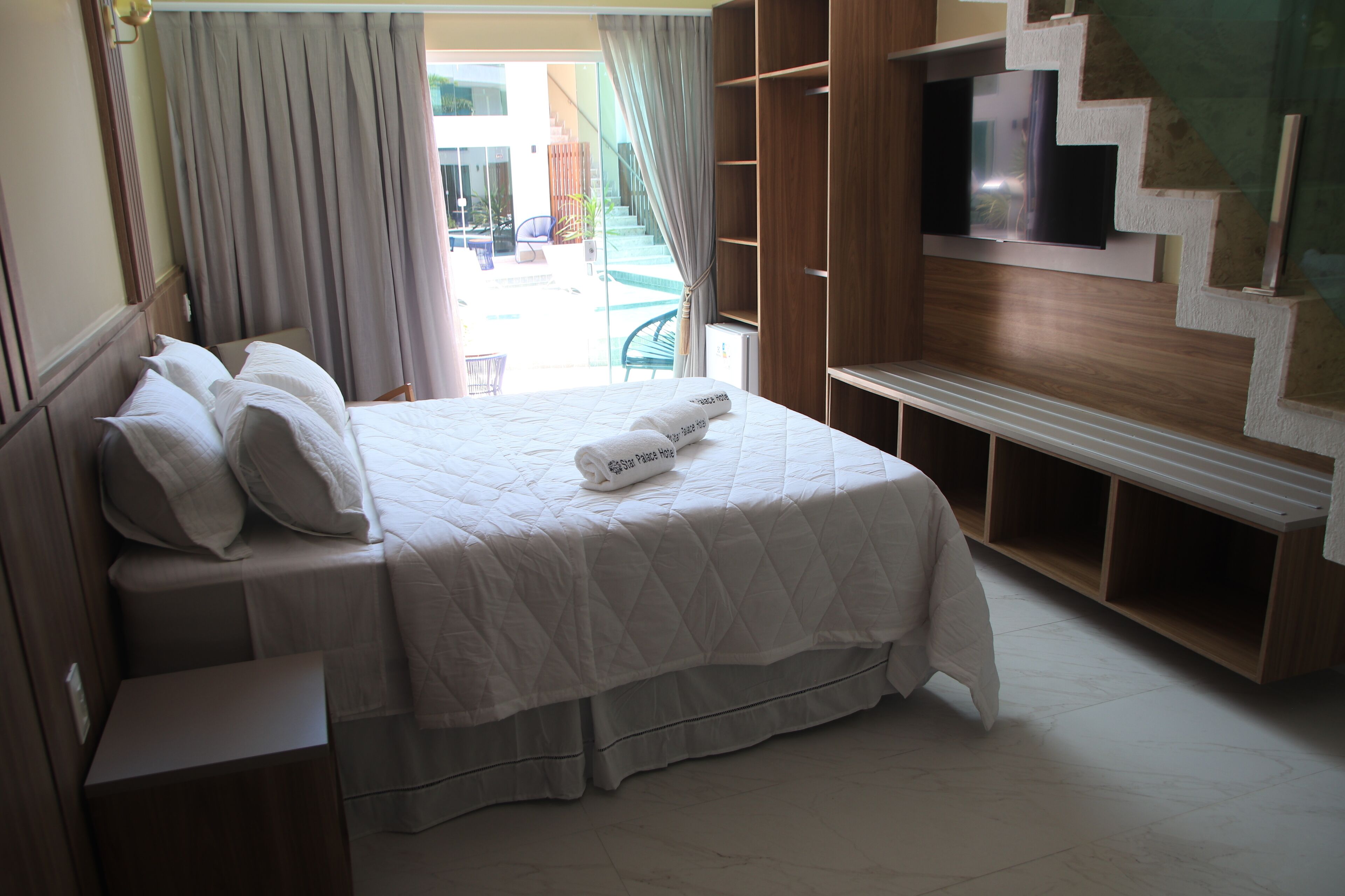 Habitación de hotel con cama, televisor montado en una pared de madera y vista al exterior.