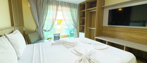 A hotel room with a large bed, a TV, a wooden wardrobe, and a balcony with a chair.
