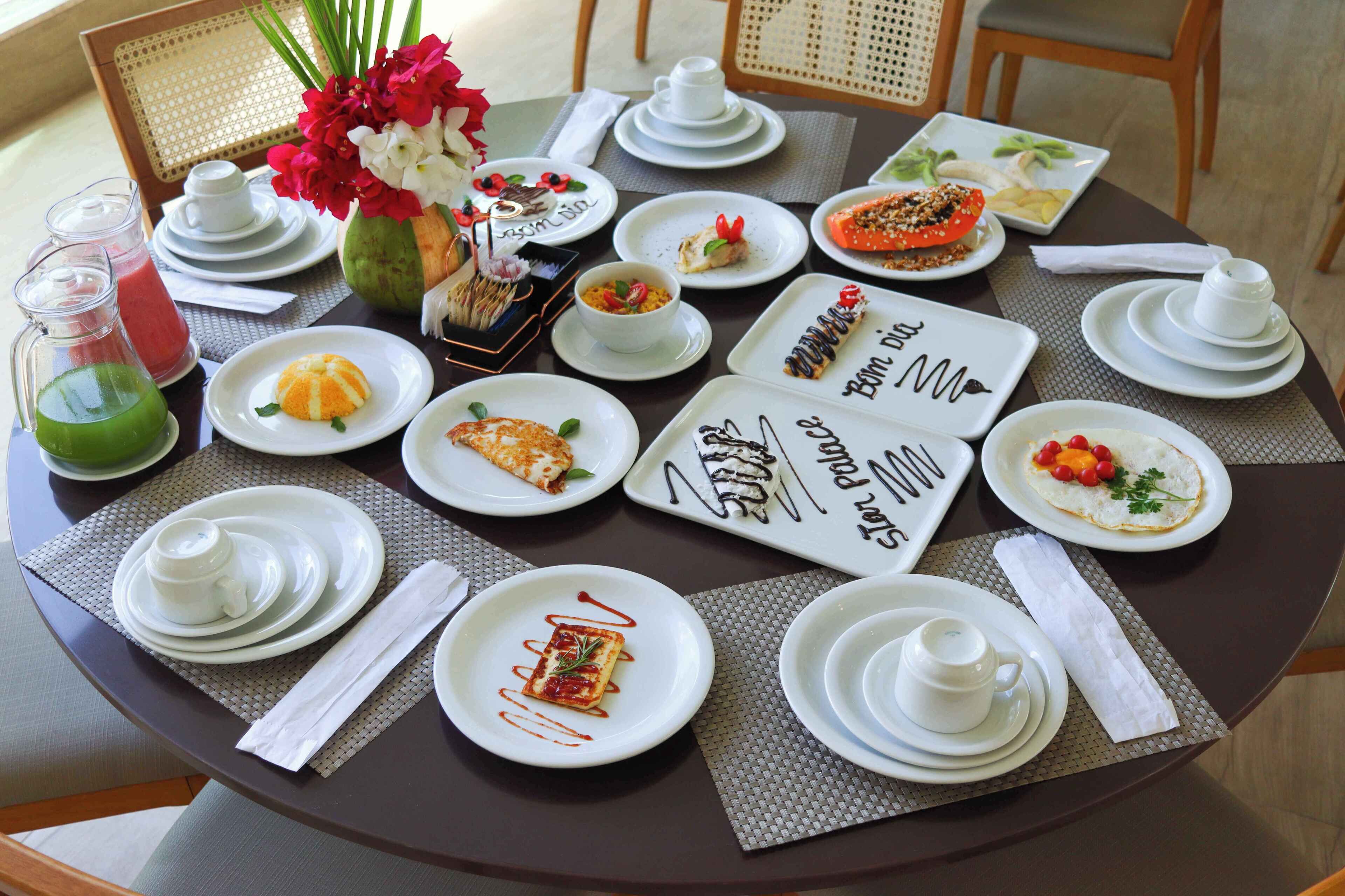 A round dining table with white plates, bowls, and cups, set with a placemat.