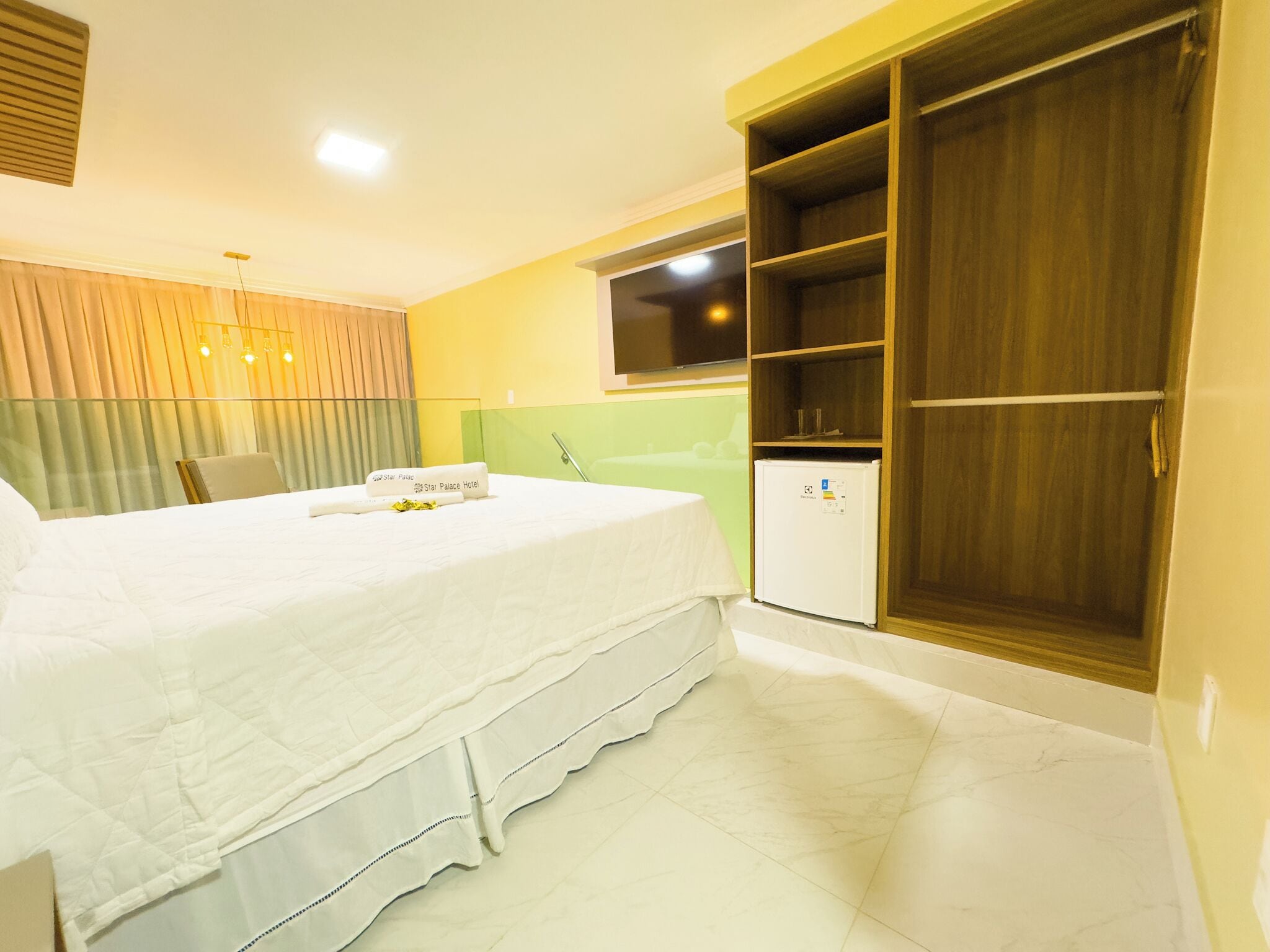 A hotel room with a bed, a wardrobe, a mini-fridge, and a chair.