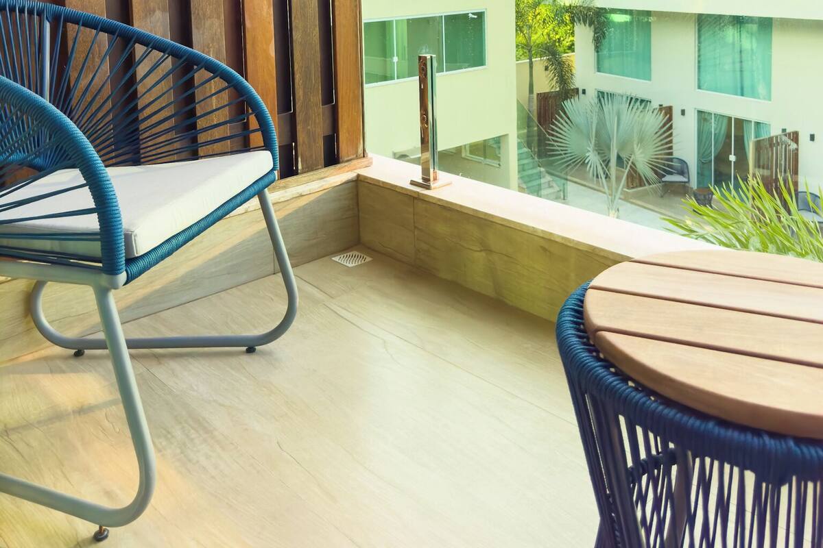 A balcony with two wicker chairs and a table, overlooking a modern building with large windows and a view of the sky.