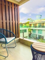 Un balcón con dos sillones de mimbre y una mesa, con vistas a un edificio moderno con grandes ventanales y el cielo.