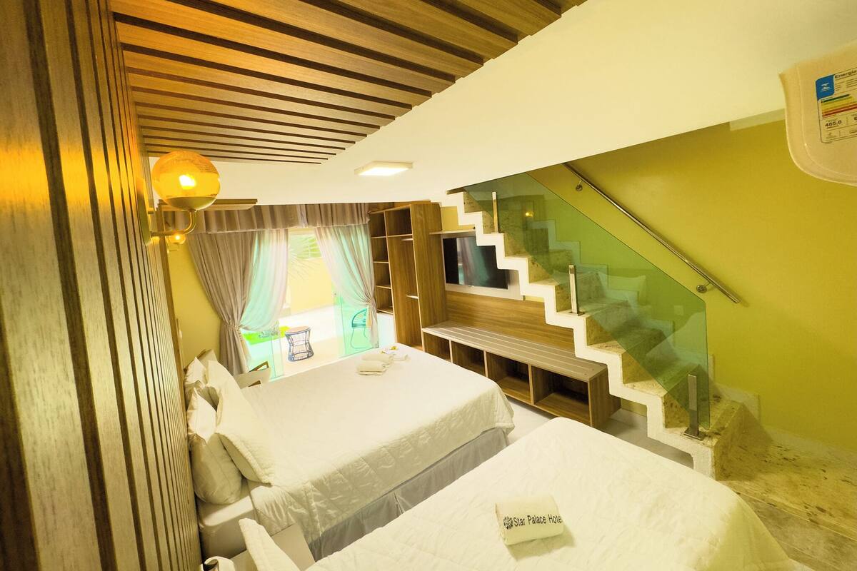 A hotel room with a bed, a desk, a chair, a staircase, and a window with curtains.