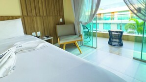 Habitación de hotel con cama, una silla, una mesita y un balcón con vistas al exterior.