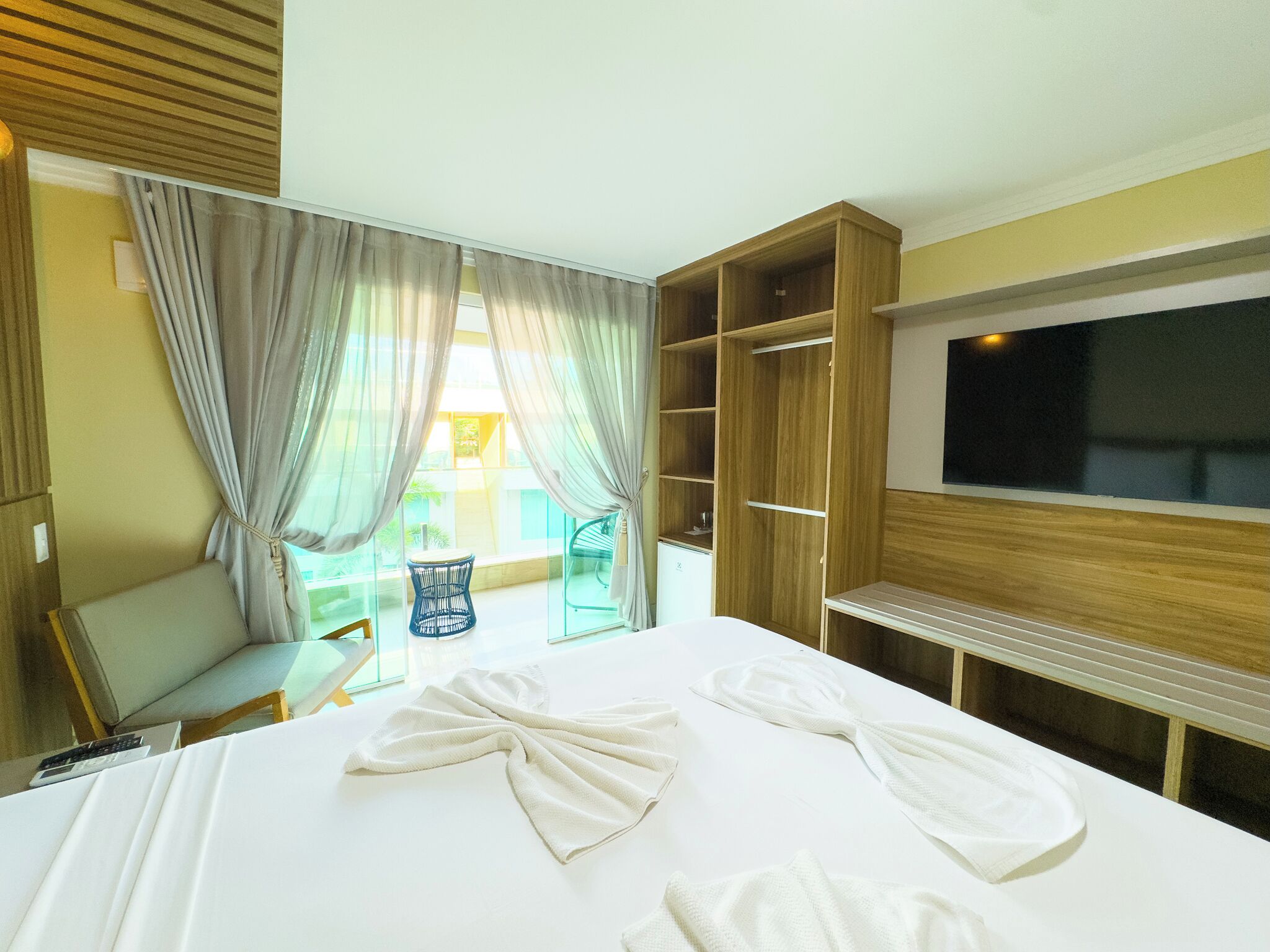 Una habitación de hotel con cama, televisión, armario y balcón con una silla y mesa.