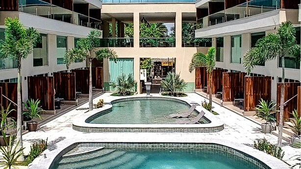 Un hotel moderno con piscina central, varias plantas y un patio con palmeras.