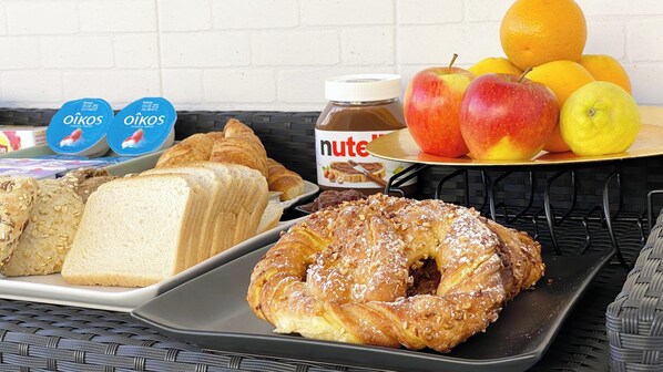 A breakfast table with bread, pastries, fruits, and a Nutella jar.