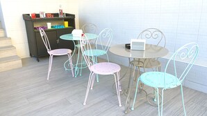 A dining area with a round table and four chairs, a small cabinet with various items, and a white brick wall in the background. - B&B Albufeira City Room Junior with Private Bathroom (Albufeira)