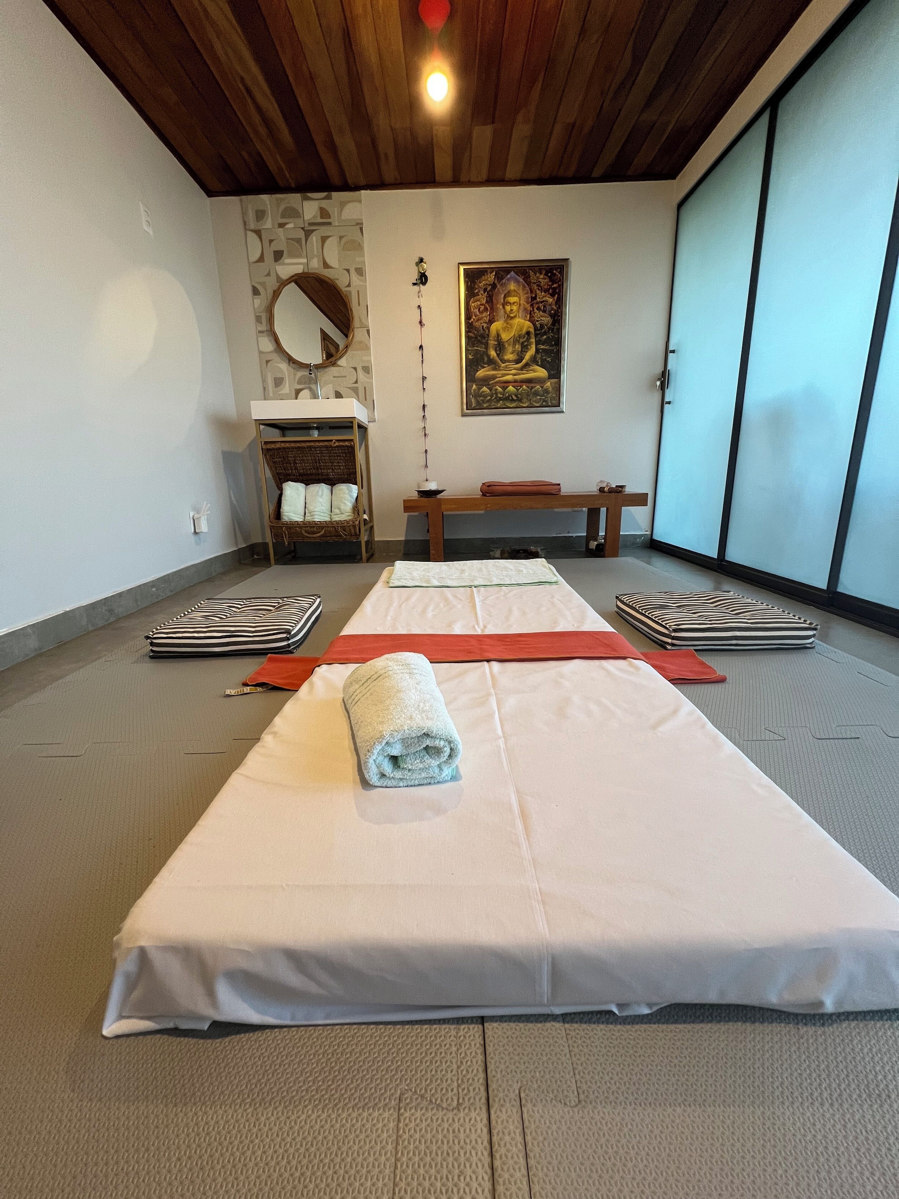 Una habitación con esteras de tatami, un banco de meditación, una estatua de Buda y un espejo en la pared.