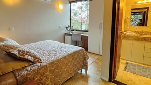 Une chambre à coucher avec un lit, un bureau et une salle de bain visible à travers une porte ouverte.