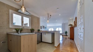 A modern kitchen with a central island, wooden cabinets, and a dishwasher. There are potted plants and a hanging light fixture. - Apartment Nautica Bay Moraira (Moraira)