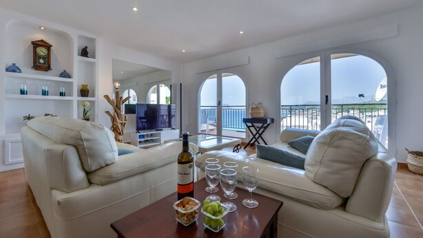A modern living room with a sofa, a coffee table with wine glasses and a bottle, and a balcony with a view. - Apartment Nautica Bay Moraira (Moraira)