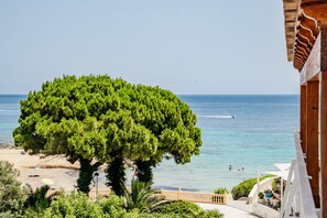 A coastal view with a large tree, beach, and a wooden building with a balcony. - Luxury Apartment Seaside Bay Moraira (Moraira)