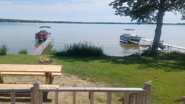 A lakeside picnic area with a wooden table and benches, docked boats, and a tree.