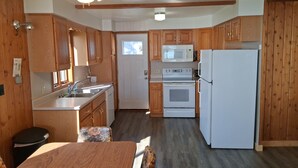 A kitchen with wooden cabinets, a microwave, a stove, a refrigerator, a ceiling fan, and a window.