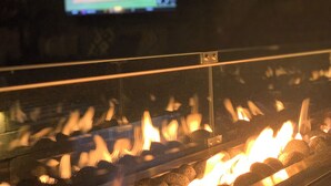 Una chimenea con llamas visibles y un televisor al fondo mostrando un partido deportivo.
