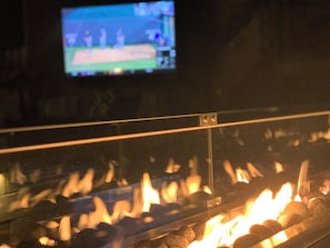 Una chimenea con llamas visibles y un televisor al fondo mostrando un partido deportivo.