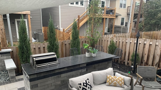 Un patio exterior con una parrilla integrada, una zona de estar con cojines y una valla de madera.