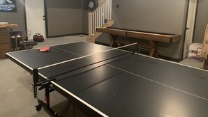 Una mesa de ping pong en una habitación con una puerta, una escalera y un letrero en la pared.