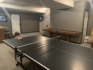 Una mesa de ping pong en una habitación con una puerta, una escalera y un letrero en la pared.