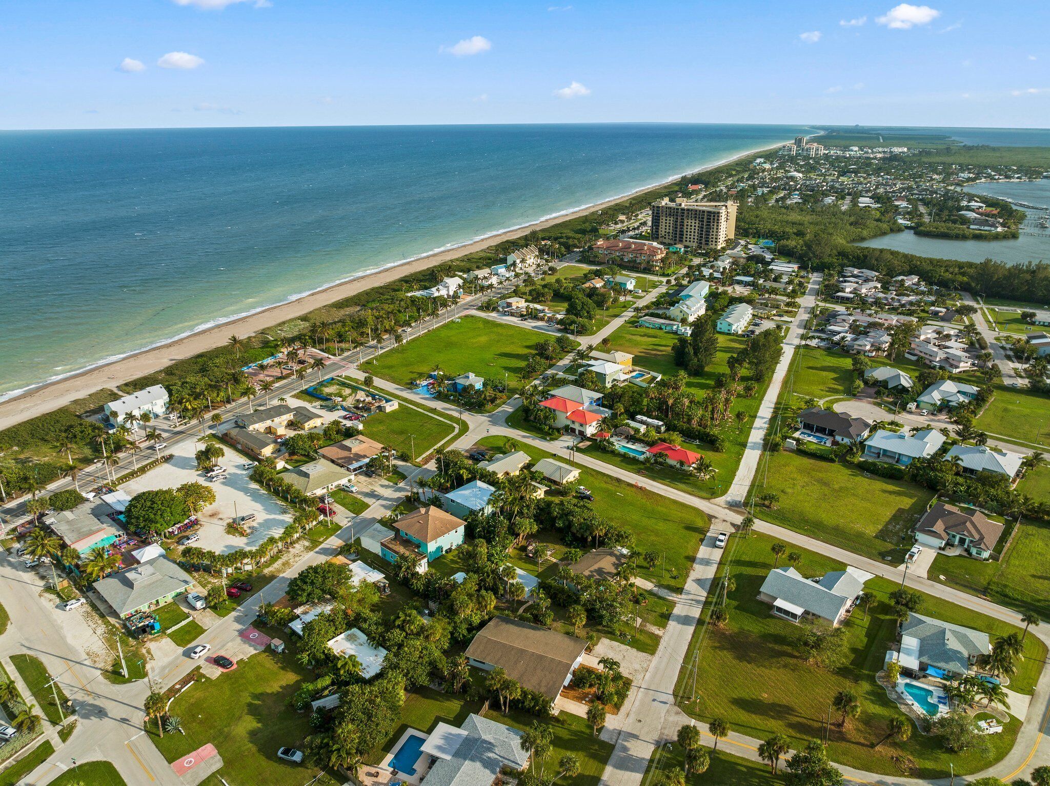 An aerial view of a coastal residential area with houses, a beach, and a large hotel.