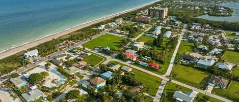 An aerial view of a coastal residential area with houses, a beach, and a large hotel.