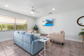 A modern living room with a blue sofa, a beige armchair, a small white table, and a TV mounted on the wall. - Mango Tree by the Sea, Hutchinson Island - Bungalow B! (Fort Pierce)