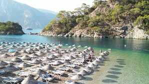 A beach with numerous sun umbrellas and lounge chairs, a clear blue sea, and a mountainous backdrop. - Sunlight Otel Fethiye (Fethiye)
