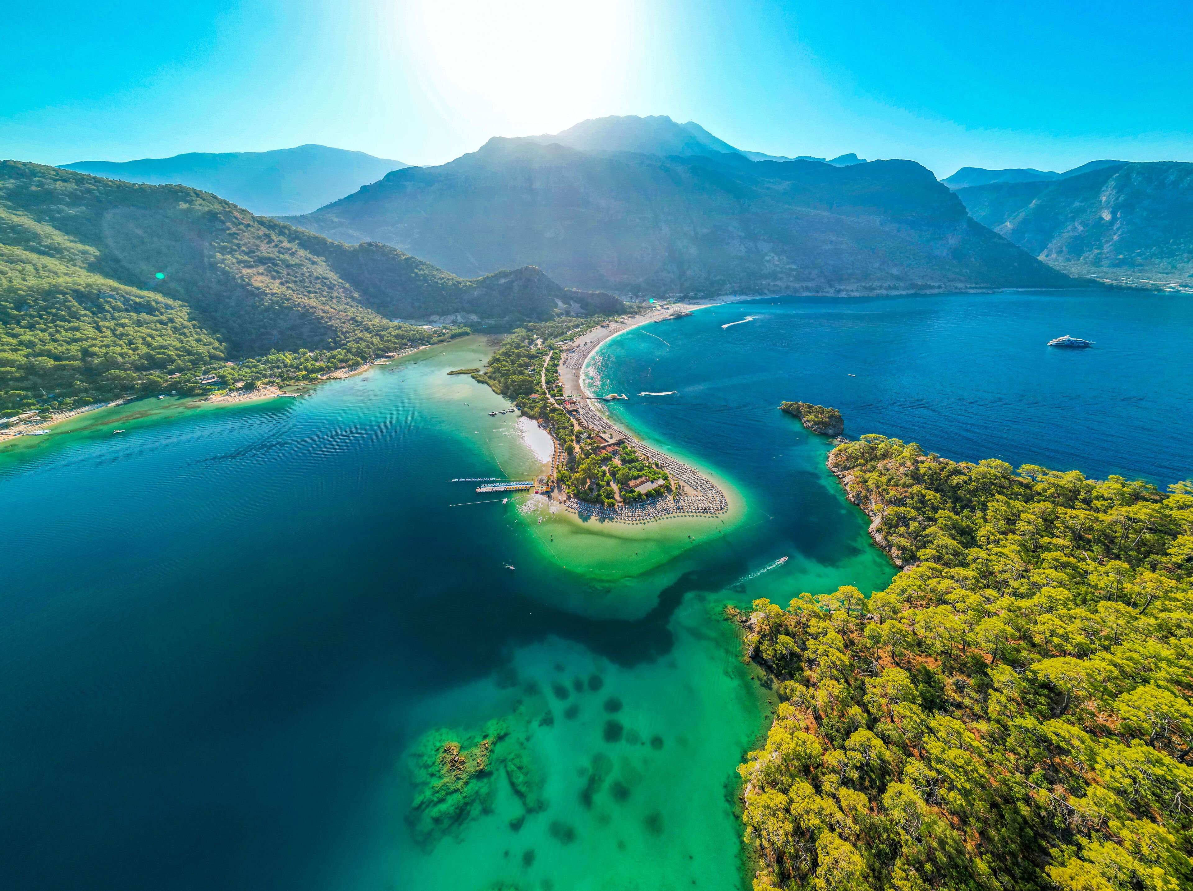 Vue aérienne d’une zone côtière avec une plage, des eaux cristallines et des collines environnantes.