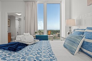 A hotel room with a bed, a window with curtains, a bedside table with a lamp, and a view of the city.