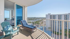 Ein Balkon mit Blick auf eine Stadtlandschaft, ein Korbsessel, ein kleiner Tisch mit einem Korb und ein blauer Stuhl mit gemustertem Sitzkissen.