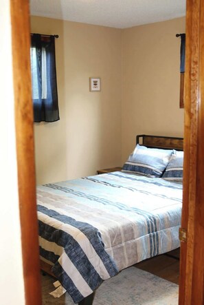 A bedroom with a bed, a wooden headboard, a single framed picture on the wall, and a window with a curtain.