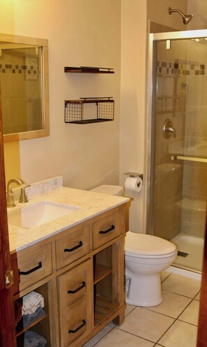 A bathroom with a sink, mirror, toilet, and shower.