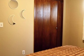 A bedroom with a wooden door, a bed with a patterned bedspread, and wall-mounted crescent mirrors.
