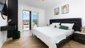 A modern bedroom with a large bed, a black headboard, and a view of the outdoors through a sliding door. - Villa Aria with heated pool & Seaview (Klimno (Krk))