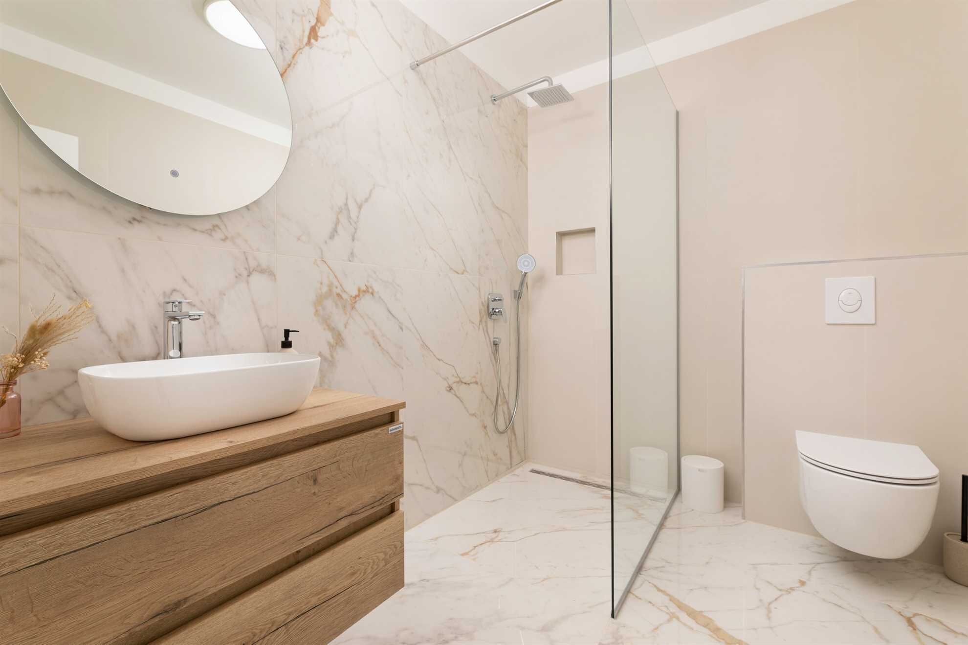 A modern bathroom with a large white sink, wooden vanity, glass shower enclosure, and a toilet.