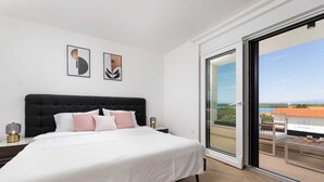Une chambre avec un grand lit, une table de chevet, une lampe et une vue sur un balcon équipé d’une table et de chaises.
