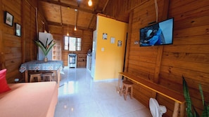 A cozy cabin interior with wooden walls, a dining area, a kitchen, and a TV mounted on the wall.
