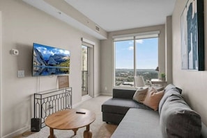 Una sala de estar moderna con un televisor grande, un sofá, una mesa redonda de centro y un balcón con vistas a la ciudad.