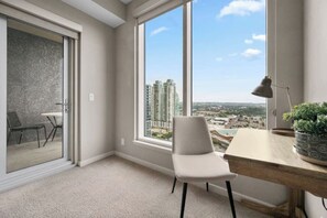 Una habitación moderna con un ventanal grande, un escritorio, una silla y vistas a edificios altos.
