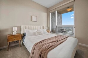 Un dormitorio con cama, mesita de noche, ventana con vistas y un cuadro en la pared.