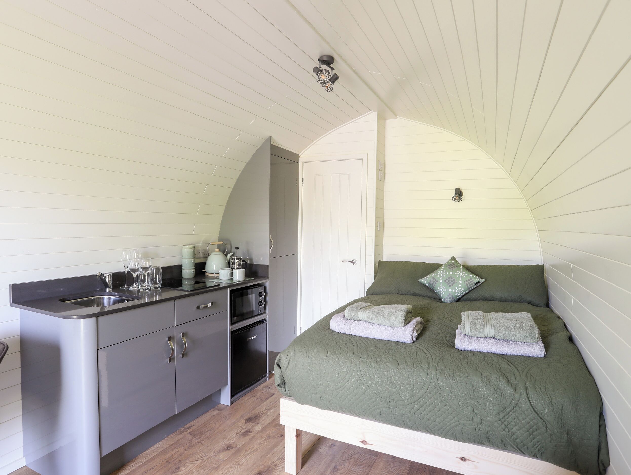 A compact bedroom with a bed, bedside tables, and a small kitchenette.