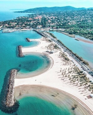 Vista aérea de una zona costera con playa, carretera y un pueblo al fondo.