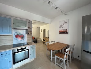 Une cuisine moderne avec un coin repas, comprenant un four encastré, un réfrigérateur et une table à manger en bois avec des chaises.