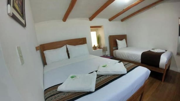 Ein Hotelzimmer mit zwei Einzelbetten, Holzbalken an der Decke, weißen Wänden und einem kleinen Fenster.