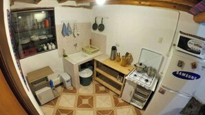 Eine kompakte Küche mit Herd, Kühlschrank und Mikrowelle. Es gibt ein Spülbecken mit einer kleinen Arbeitsfläche und ein Fenster darüber.